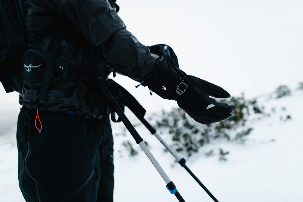 Fokus auf Zanier Handschuhe, Mann mit Winterausrüstung in verschneiter Landschaft.
